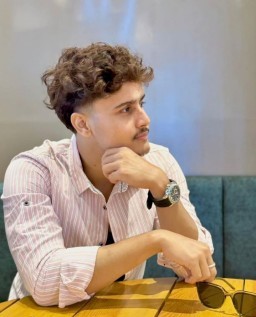 HICH:With curly hair and a striped shirt, sitting at a table, looking thoughtfully.